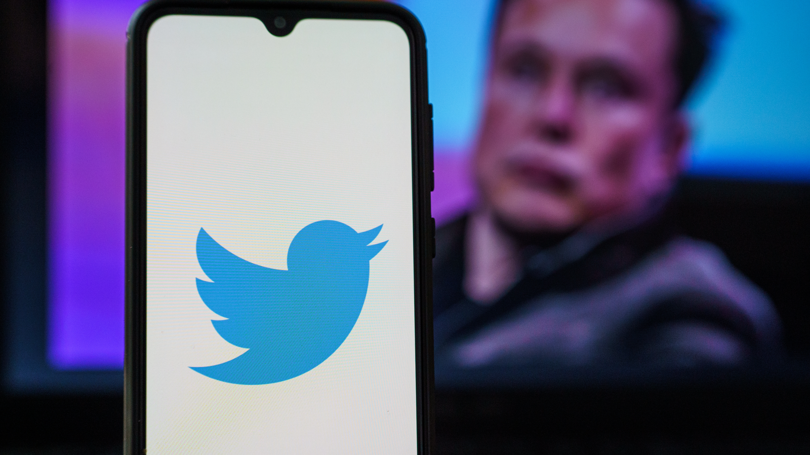 Twitter Layoffs (TWTR) logo on smartphone and Elon Musk in the background.