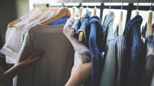 A photo of someone looking at clothing on hangers, hanging from a rack.