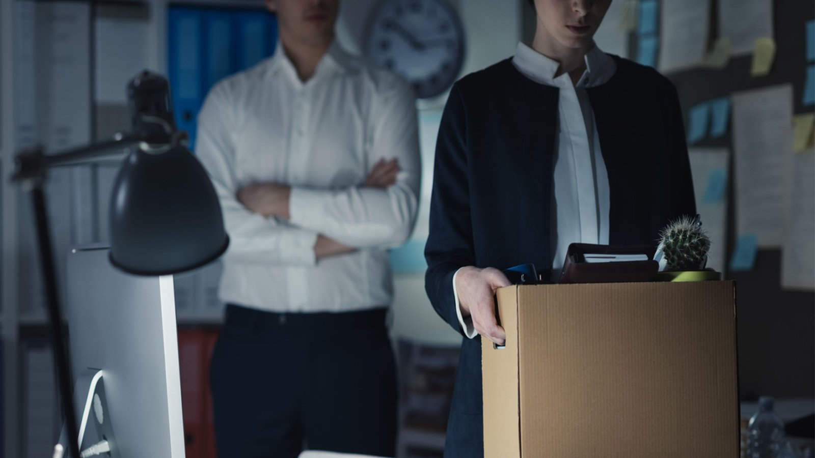 A woman leaving an office with her things in a box representing layoffs.