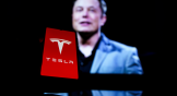 Tesla, Inc. (TSLA) logo displayed on a phone in front of a blurred image of Elon Musk. Tesla layoffs
