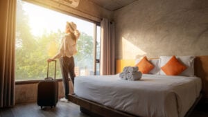 Woman standing in hotel room with luggage looking at view. Hotel stocks.