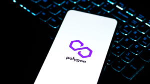 A phone, on top of a laptop keyboard, displaying the logo for Polygon