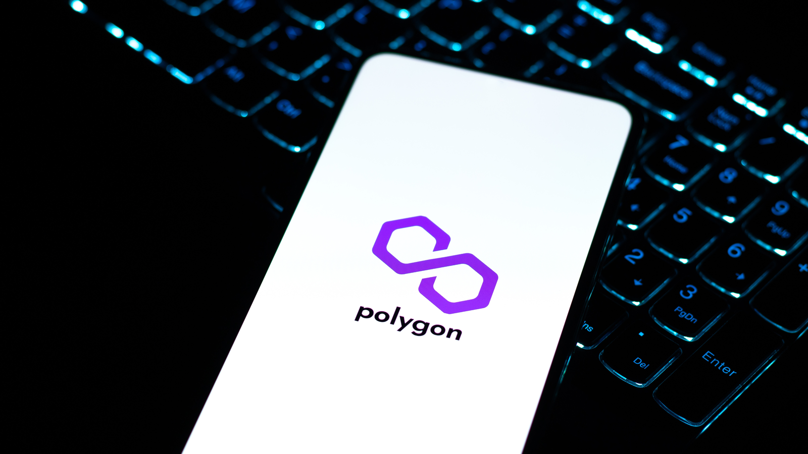 A phone, on top of a laptop keyboard, displaying the logo for Polygon (MATIC-USD) representing Polygon Price Predictions.