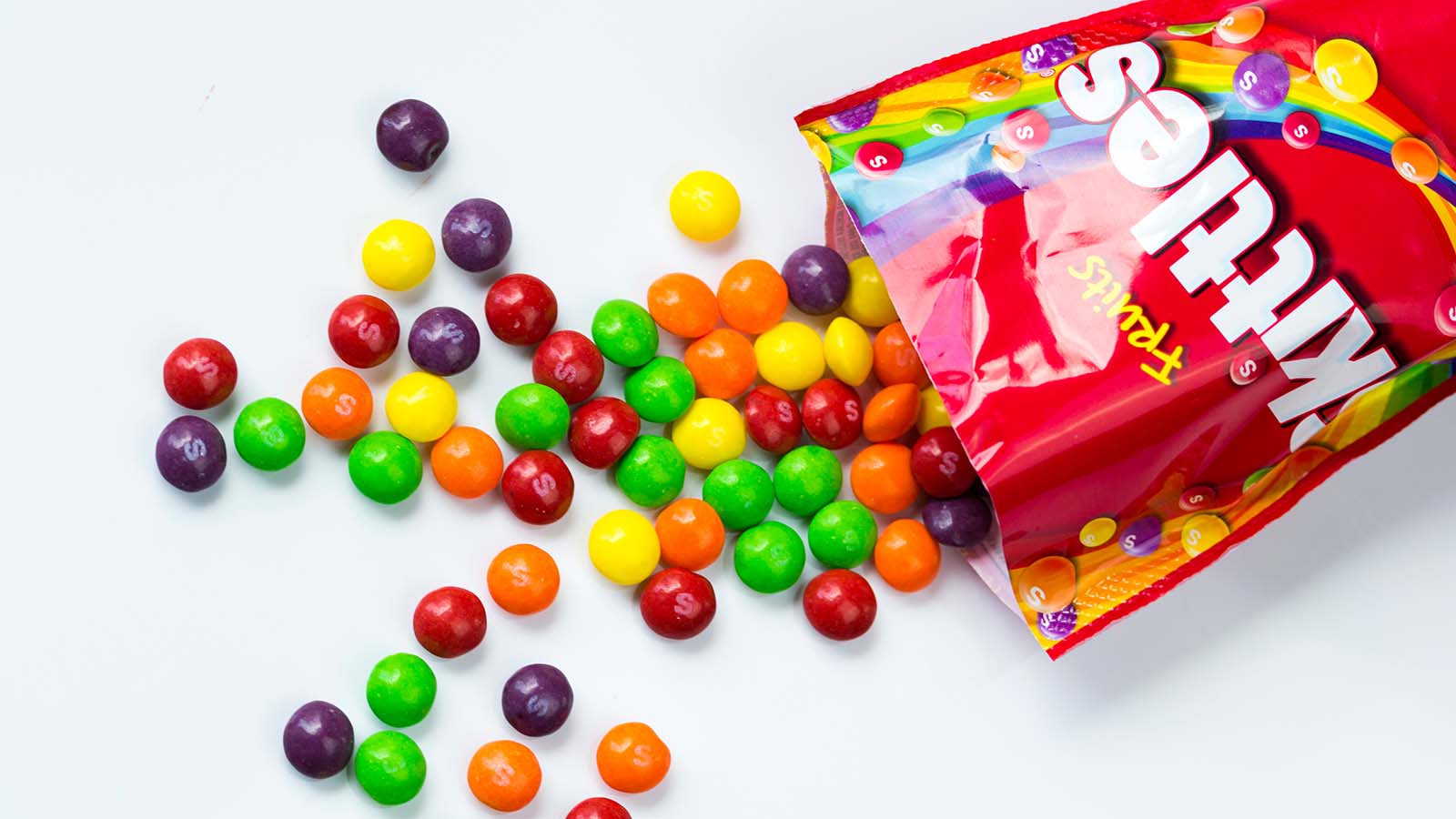 A red bag of skittles is spilled out across a white flat surface representing the candy lawsuit.