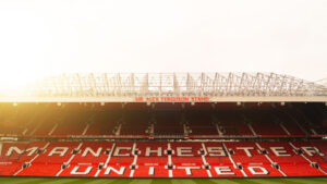 Wide shot photo of Manchester United (MANU) stadium seating at sunset, red seats with white text reading "Manchester United"