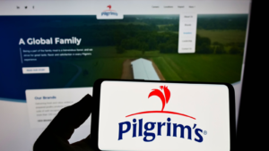 Person holding smartphone with logo of US food company Pilgrim's Pride Corporation on screen in front of website. Focus on phone display. Unmodified photo. PPC stock