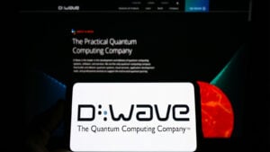 QBTS stock: Person holding mobile phone with logo of Canadian hardware company D-Wave Systems Inc. on screen in front of web page.