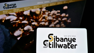 ウェブサイトの前の画面に南アフリカの鉱山会社 Sibanye Stillwater Limited のロゴが表示されたスマートフォンを持っている人。電話のディスプレイに注目してください。無修正の写真。