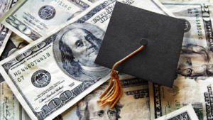 Black college graduation cap laying on a pile of $100 and $20 dollar bills