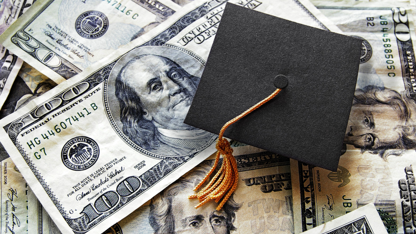 Black college graduation cap laying on a pile of $100 and $20 dollar bills representing ZVO Stock.