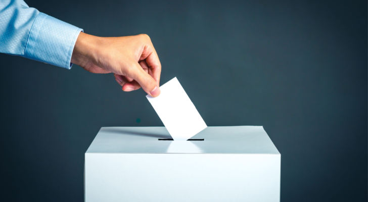 An image of a hand putting a ballot in a ballot box; voting in an election