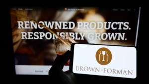 Person holding cellphone with logo of American spirits company Brown-Forman (BF-B) Corporation on screen in front of webpage. Focus on phone display. Unmodified photo.