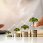 A businessman holding a coin with a tree that grows and a tree that grows on a pile of money representing growth stocks. top growth stocks