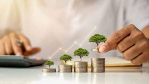 A businessman holding a coin with a tree that grows and a tree that grows on a pile of money representing growth stocks