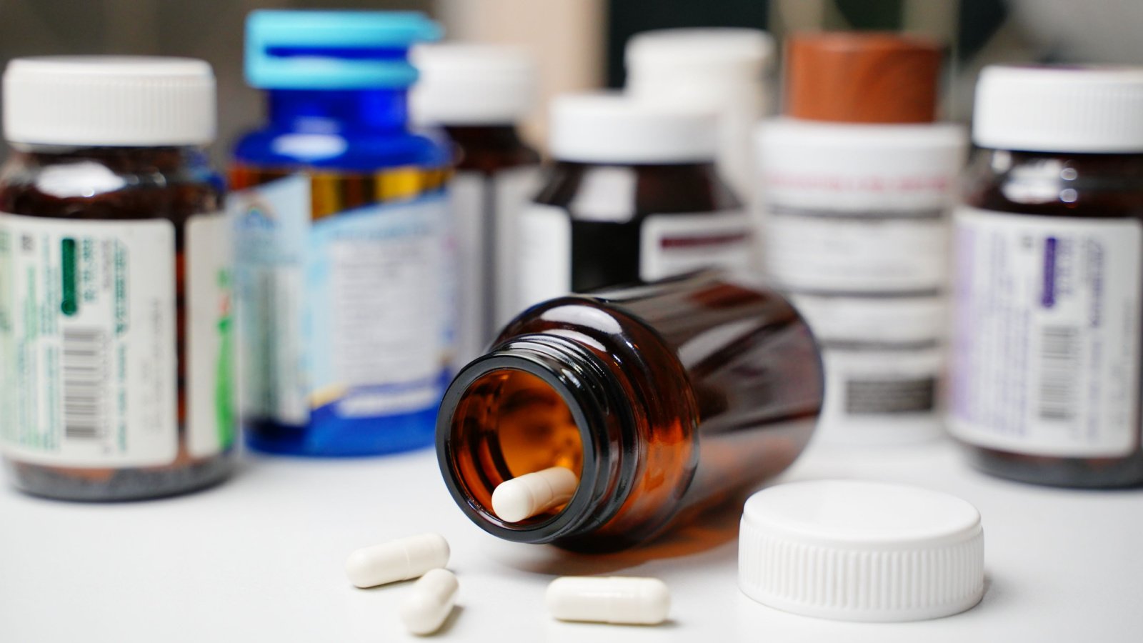 Brown glass pill bottle on its side showing white pills inside, with other pill bottles behind it representing ATNX stock.