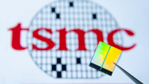 微芯片（又名半导体芯片、半导体器件、集成电路）用镊子固定的特写照片，背景上有台积电 (TSM) 徽标。