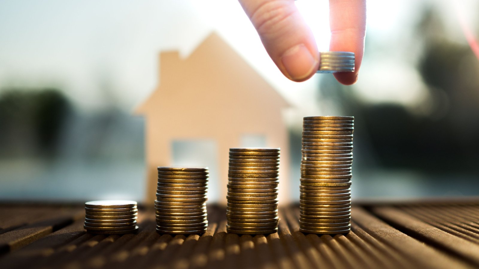 Coins stacked in front of graphic 2D cutout of house with sunlight shining on coins