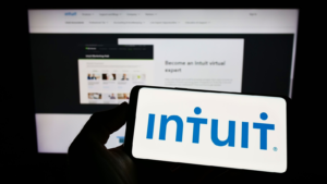 Person holding cellphone with logo of US financial software company Intuit Inc. (INTU) on screen in front of business webpage. Focus on phone display. Unmodified photo.