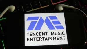 Closeup of smartphone screen with logo lettering of tencent music (TME) online music streaming service on computer keyboard (focus on center of upper black lettering)