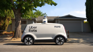 An image of an Uber Eats' Nuro self-driving vehicle parked on the street, a tree and home in the background