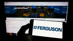 Person holding mobile phone with logo of British company Ferguson (FERG) plc on screen in front of business web page. Focus on phone display. Unmodified photo.