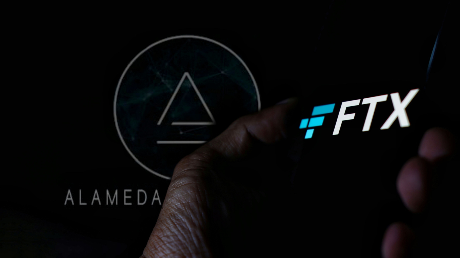 FTX logo displayed on phone held in hand, with Alameda Research logo in background