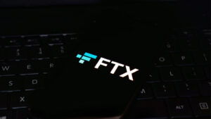 FTX ロゴがスマートフォンに表示され、背景が黒色でスマートフォンが黒色のキーボードに置かれている