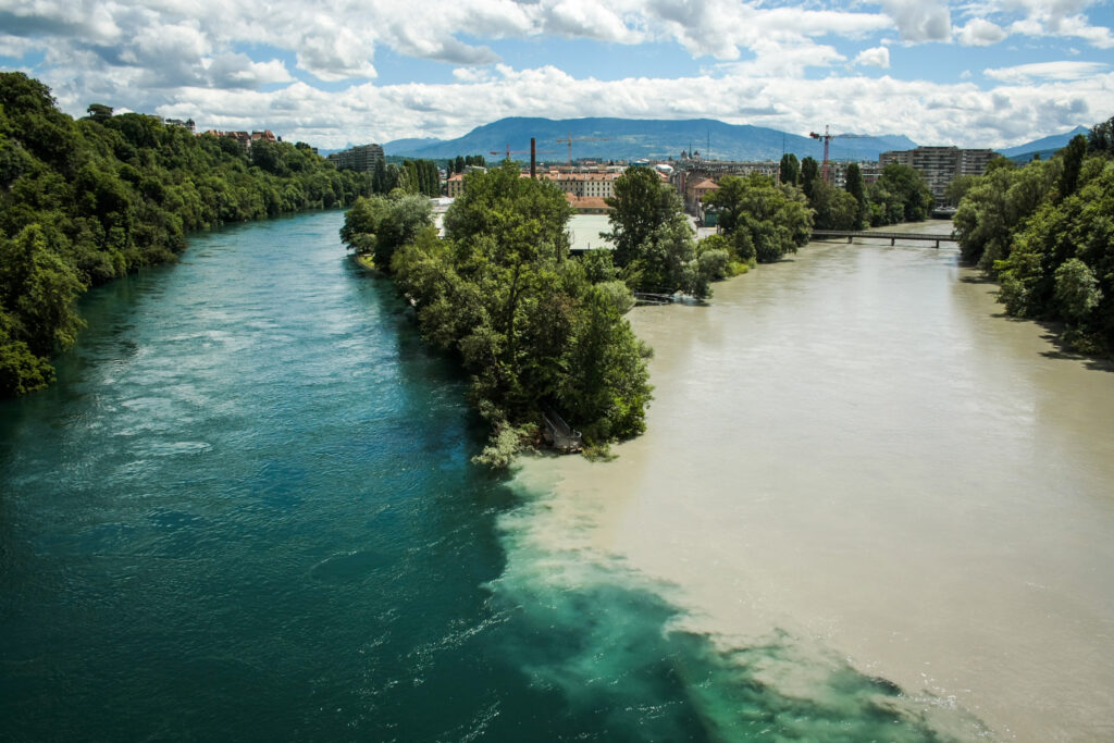 A view of the river Rhone and river Arve at Jonction in Geneve from the rail bridge. You can see the city and the mountains in the background.