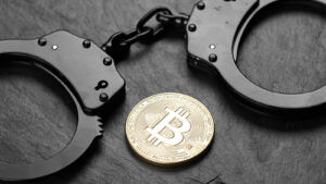 Black handcuffs laid next to Bitcoin on black slate background symbolizing crypto law and crypto-related arrest