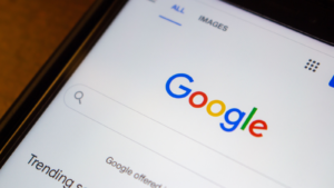 Close-up of the Google.com website logo on an iPhone on a wooden table.  GOOG Stock and Layoffs at Google