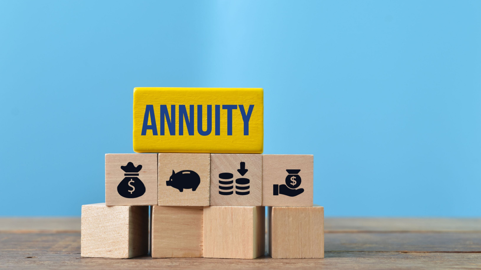 The word "annuity" displayed on a big yellow block and symbols signifying saving money on smaller blocks, including a money bag, a piggy bank, coins and a hand with a small jar of money