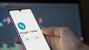 A hand holding a phone showing the Bitget Token logo and name (BGB).