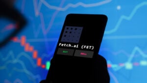 Fetch.AI (FET) crypto logo displayed on smartphone with words "buy" and "sell" below logo and financial chart in background
