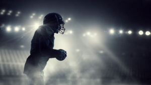 Football player holding football in dark stadium with stark lighting
