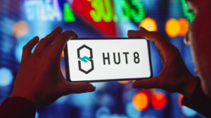 Hut 8 (HUT) logo displayed on a phone screen with colorful market chart in the background