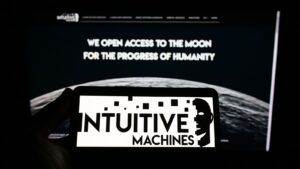 Intuitive Machines (LUNR) black and white logo displayed on smartphone screen with desktop screen behind it showing company website and image of moon