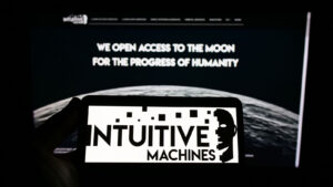 Intuitive Machines (LUNR) の白黒のロゴがスマートフォンの画面に表示され、その背後にデスクトップ画面が表示され、会社の Web サイトと月の画像が表示されます