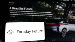 Person holding mobile phone with logo of electric vehicle company Faraday Future (FFIE) on screen in front of web page. Focus on phone display. Unmodified photo.