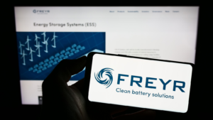 Person holding smartphone with logo of Norwegian battery company Freyr AS (FREY) on screen in front of website. Focus on phone display. Unmodified photo.