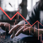 Grayish photo of investor's hands hovering over laptop with red stock graph showing downward arrow overlayed on top of the image. falling stocks. Blue-chip stocks to sell