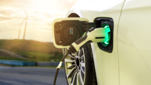 Electric car or EV car charging in station on blurred of sunset with wind turbines in front of car on background. Eco-friendly alternative energy concept