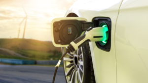 Electric car or EV car charging in station on blurred of sunset with wind turbines in front of car on background. Eco-friendly alternative energy concept. best battery stocks to buy