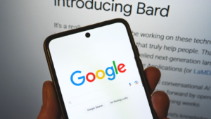 Google launches Bard AI. Google search bar on a phone in hand with release information on background. Google Bard AI vs OpenAI ChatGPT. GOOG stock and GOOGL stock.