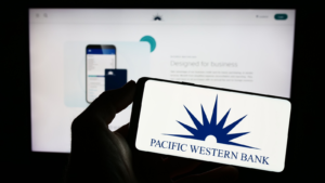 Person holding mobile phone with logo of American banking company PacWest Bancorp (PACW) on screen in front of business web page. Focus on phone display. Unmodified photo
