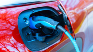 Closeup photo of red electric vehicle being charged with blue and black charger plugged into charging port