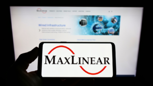 A hand holding a phone that shows the MaxLinear (MXL) logo. 