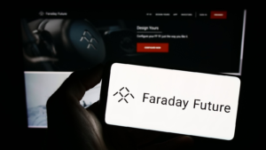 Person holding cellphone with logo of electric vehicle company Faraday Future Inc. (FFIE) on screen in front of business webpage. Focus on phone display. Unmodified photo.