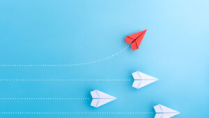 Image of white paper airplanes on horizontal trajectory with one red paper airplane rising upward, symbolizing growth stocks