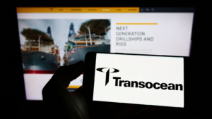 Person holding smartphone with logo of offshore drilling company Transocean Ltd. (RIG) on screen in front of website. Focus on phone display. Unmodified photo.