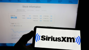 Person holding mobile phone with logo of US broadcasting company Sirius XM Holdings Inc. (SIRI) on screen in front of web page. Focus on phone display. Unmodified photo.